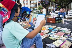 Foto con niño sentado de perfil leyendo un libro en una feria de trueque de libros en Colombia.