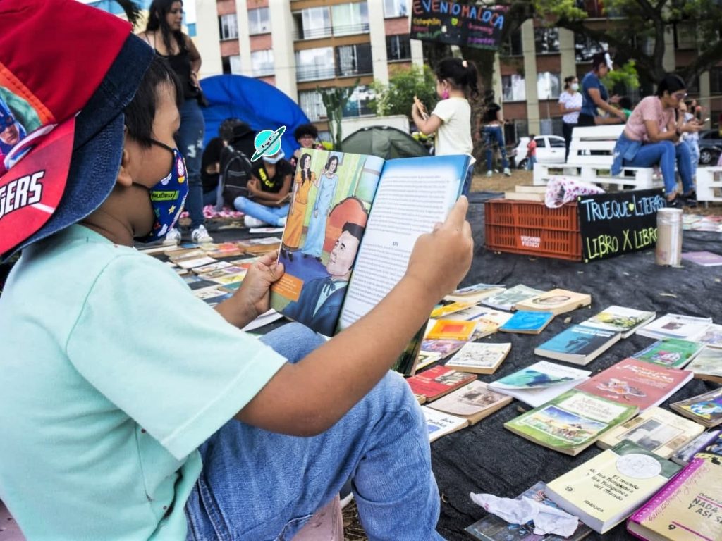 Foto con niño sentado de perfil leyendo un libro en una feria de trueque de libros en Colombia.