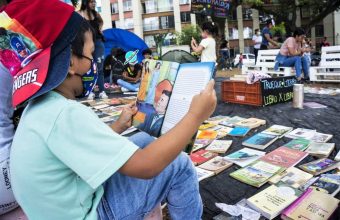 Foto con niño sentado de perfil leyendo un libro en una feria de trueque de libros en Colombia.